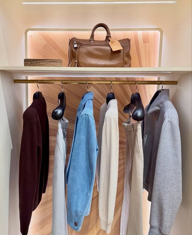 Styling guide: brown leather Trunk Edition 2026 handbag on a store shelf above hanging knitwear and tailoring